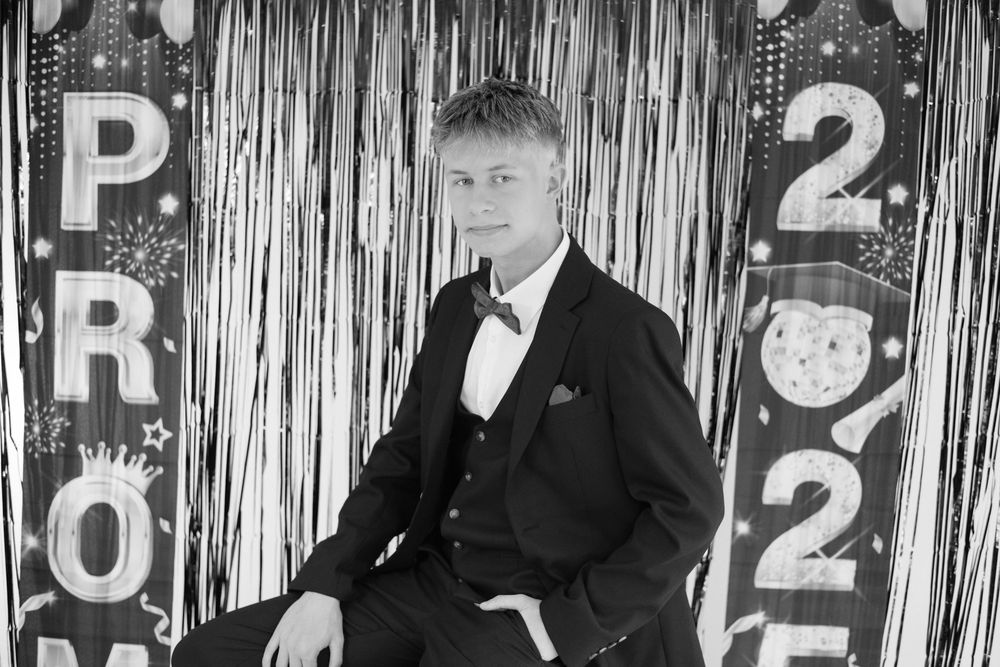 Formal portrait against silver tinsel backdrop with young man in black tuxedo and bow tie.