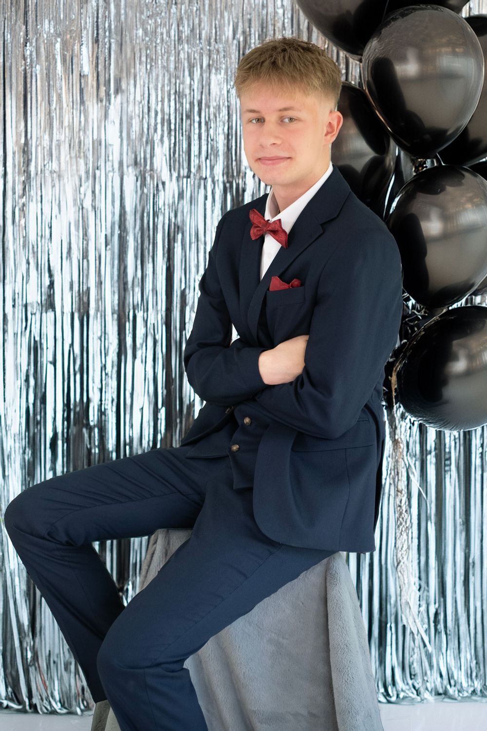 Stylish portrait with black balloons and silver tinsel backdrop featuring suited gentleman.