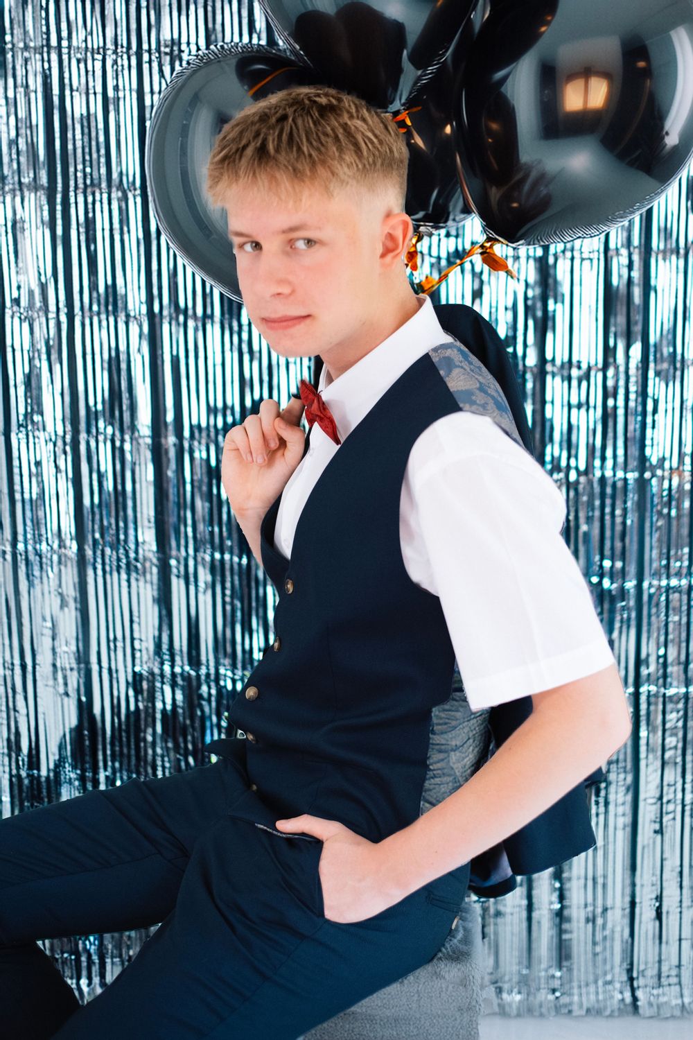 A portrait against a silver tinsel backdrop with black balloons and formal attire.