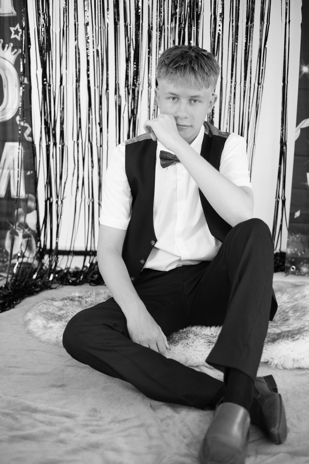 Black and white photo of seated person in formal wear against silver streamer background.