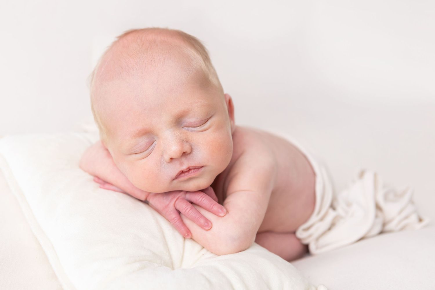 Peaceful sleeping newborn baby swaddled in white blankets against a light background.