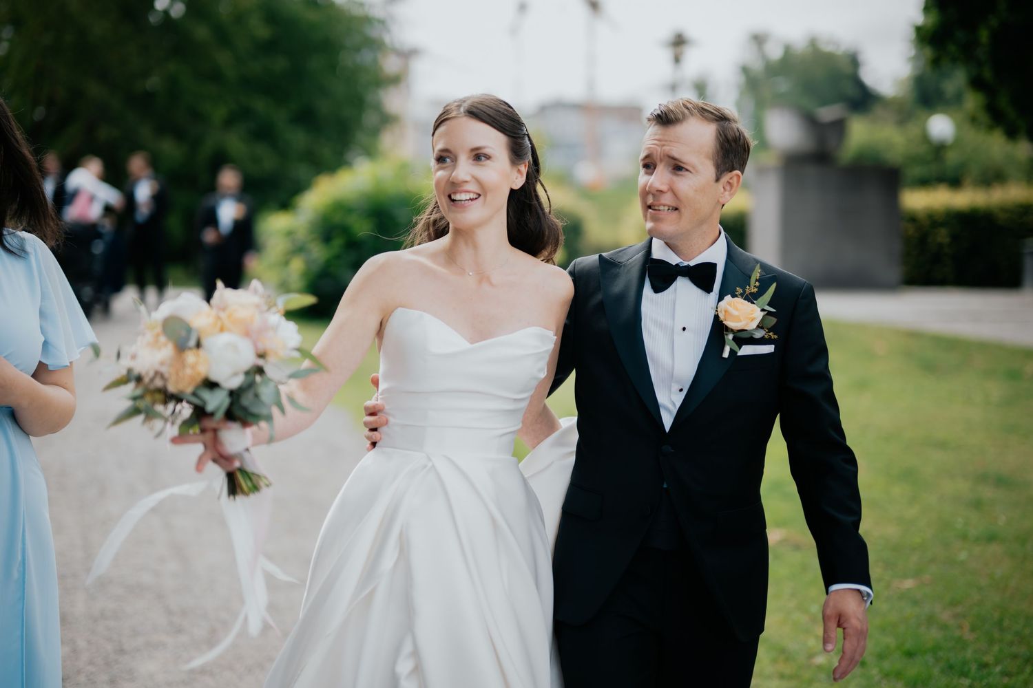 A formal wedding couple walks together on lush green grass holding floral bouquets on their special day.