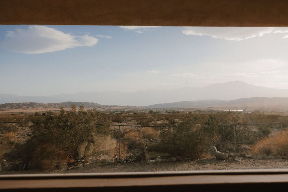 Desert landscape viewed through car window with scrub brush and mountains in hazy distance during sunset.