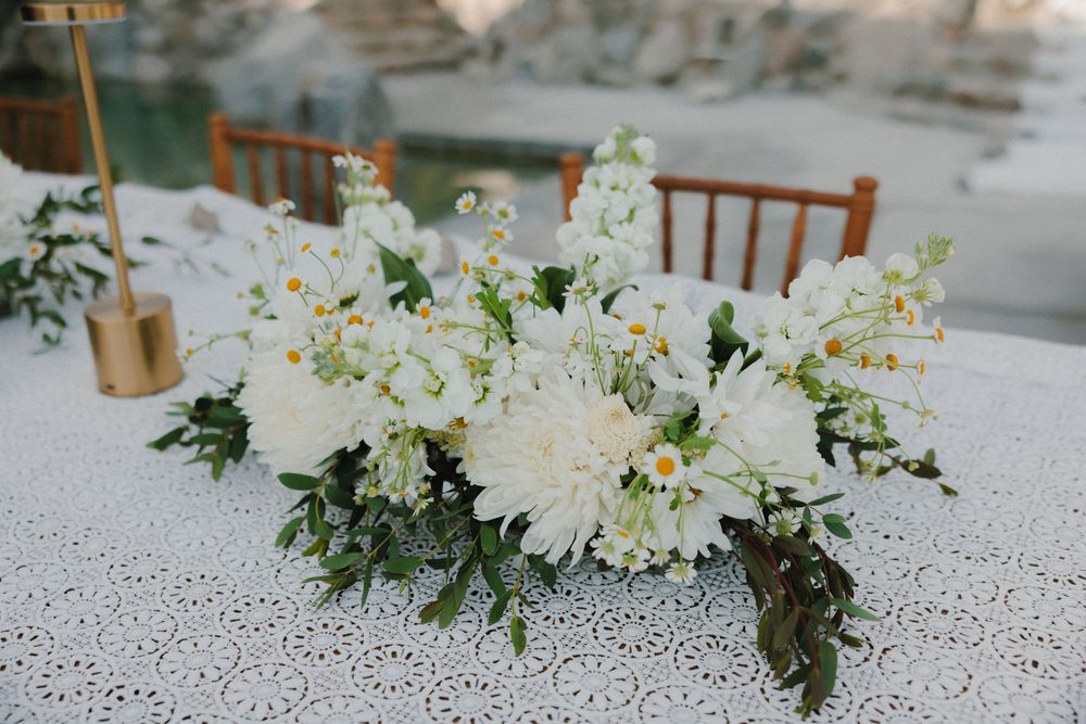 White floral wedding centerpiece arrangements adorn a rustic reception table with matching white linens and greenery accents.