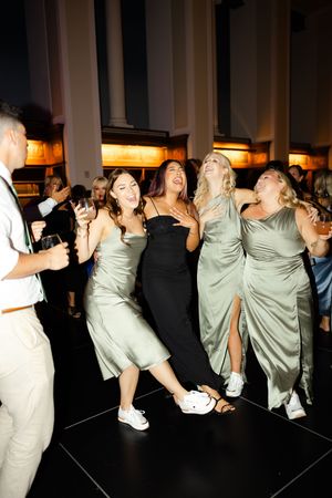 Group of people in mint green outfits performing dynamic dance moves in a dimly lit indoor space.