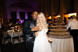 A multi-tiered champagne tower is displayed at an elegant wedding reception with warm lighting and party atmosphere.