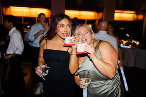 Two friends enjoying colorful cocktails together at a party with ambient lighting in the background.