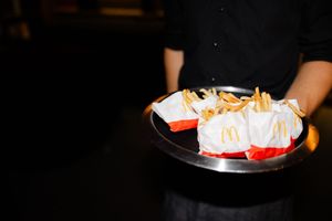Beautifully plated appetizers and desserts on dark plates being served at an event.