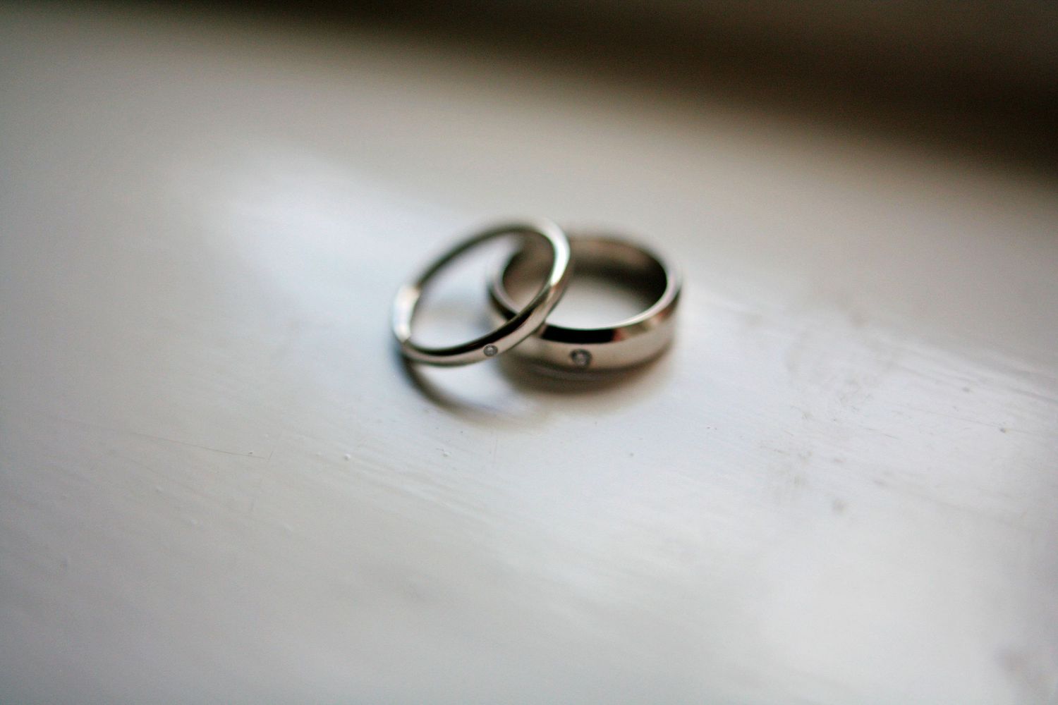 Wedding rings photographed on light gray surface with dramatic lighting.