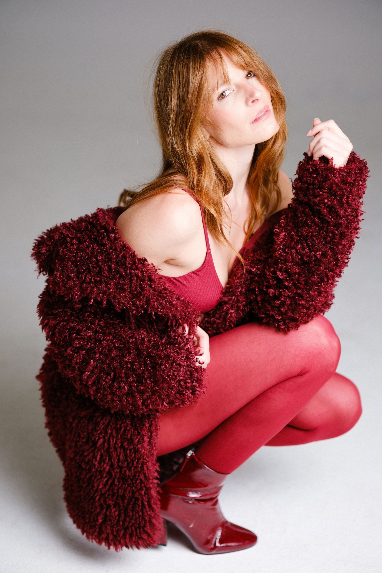 Fashion model in burgundy outfit creates dynamic poses against studio backdrop.