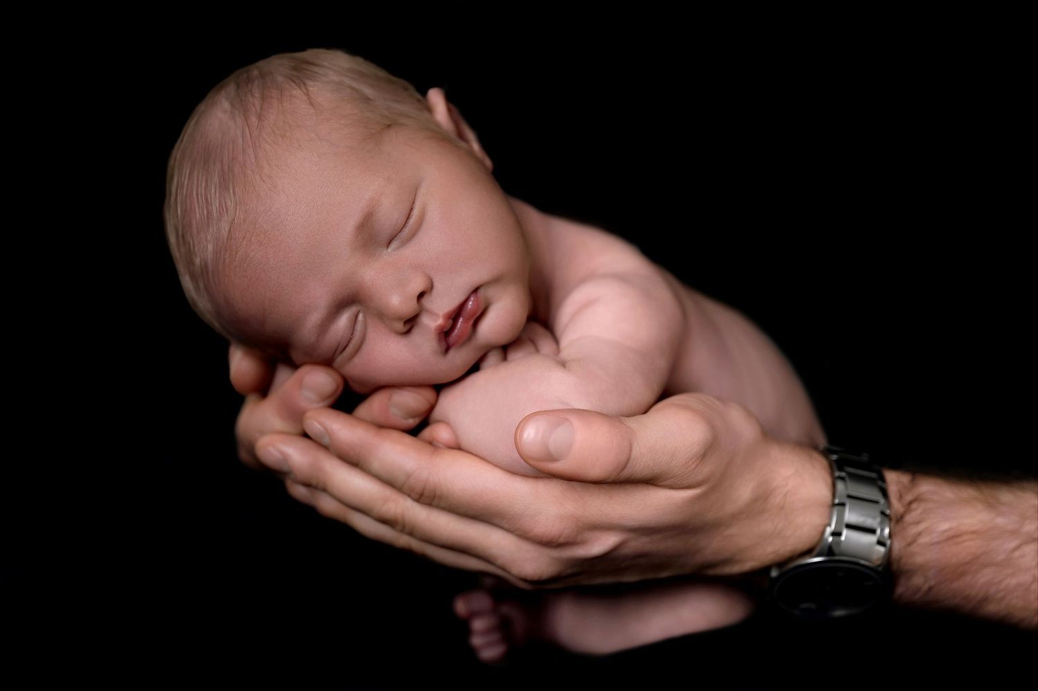 Artistic portrait of sleeping newborn gently cradled in hands against dark background.