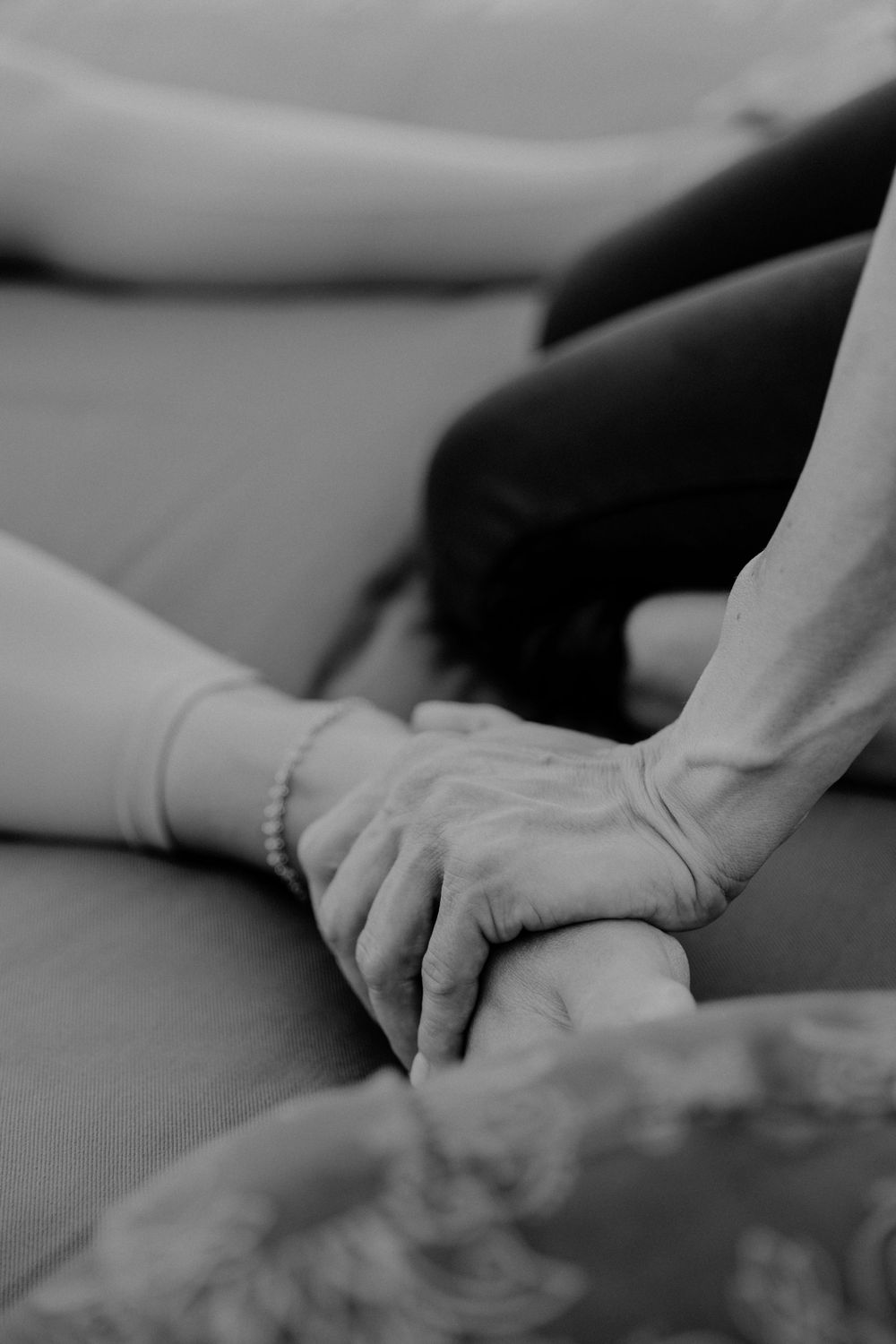 Black and white close-up shot of two hands tenderly holding each other against a soft fabric surface.
