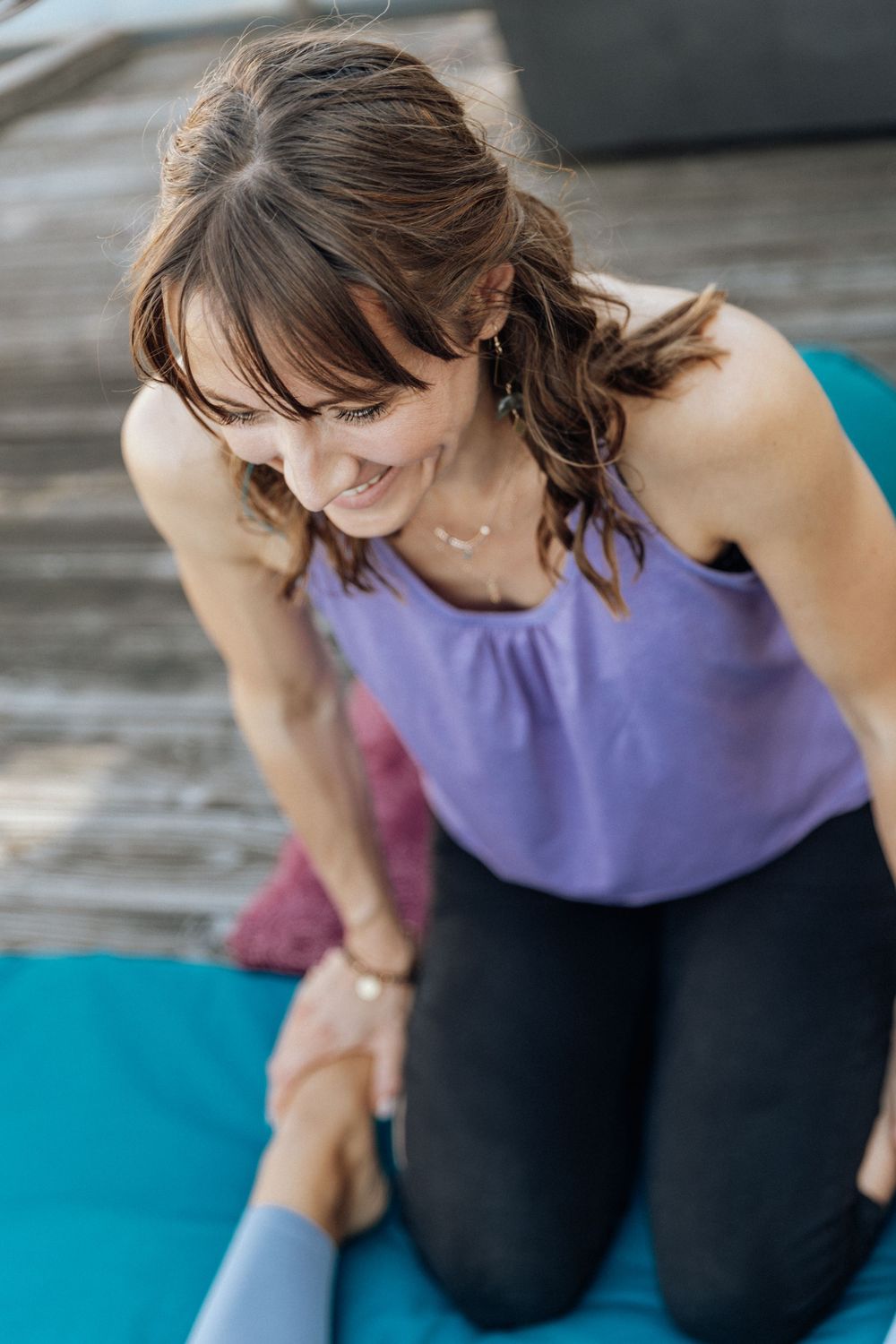 Person wearing purple tank top and black leggings kneels on a blue yoga mat during exercise session.