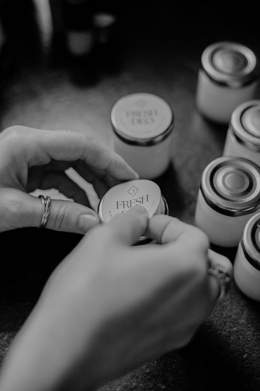Hands holding jar lids marked 'Fresh' with multiple mason jars in black and white photography.