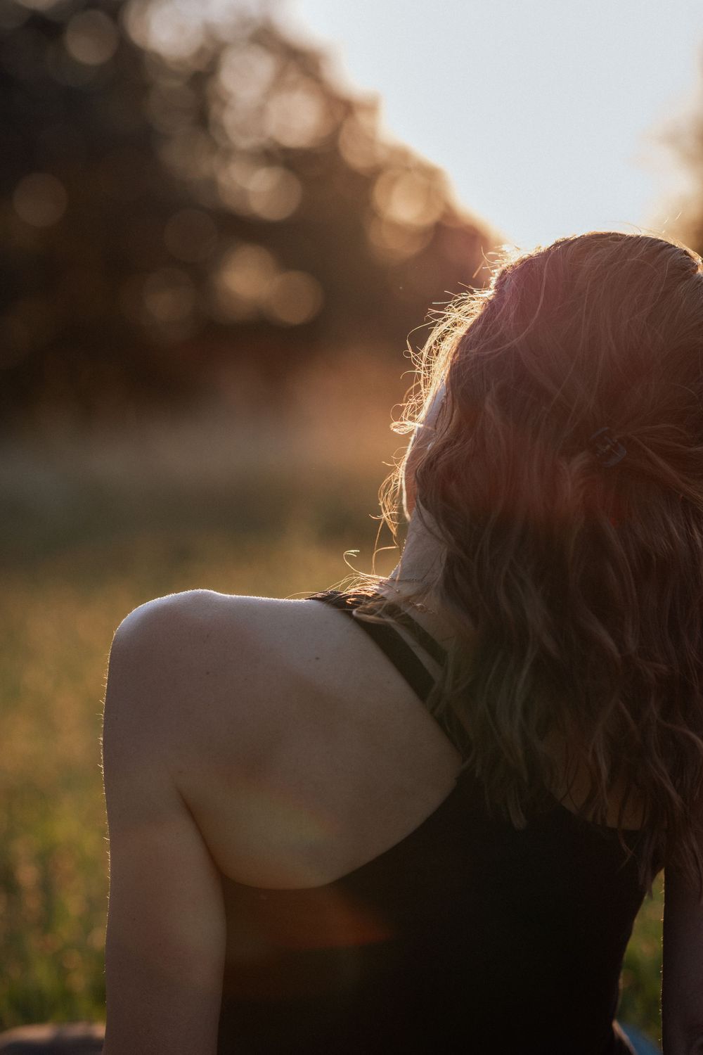 A person with wavy hair sits outside during golden hour with sunlight creating a warm backlit silhouette effect.