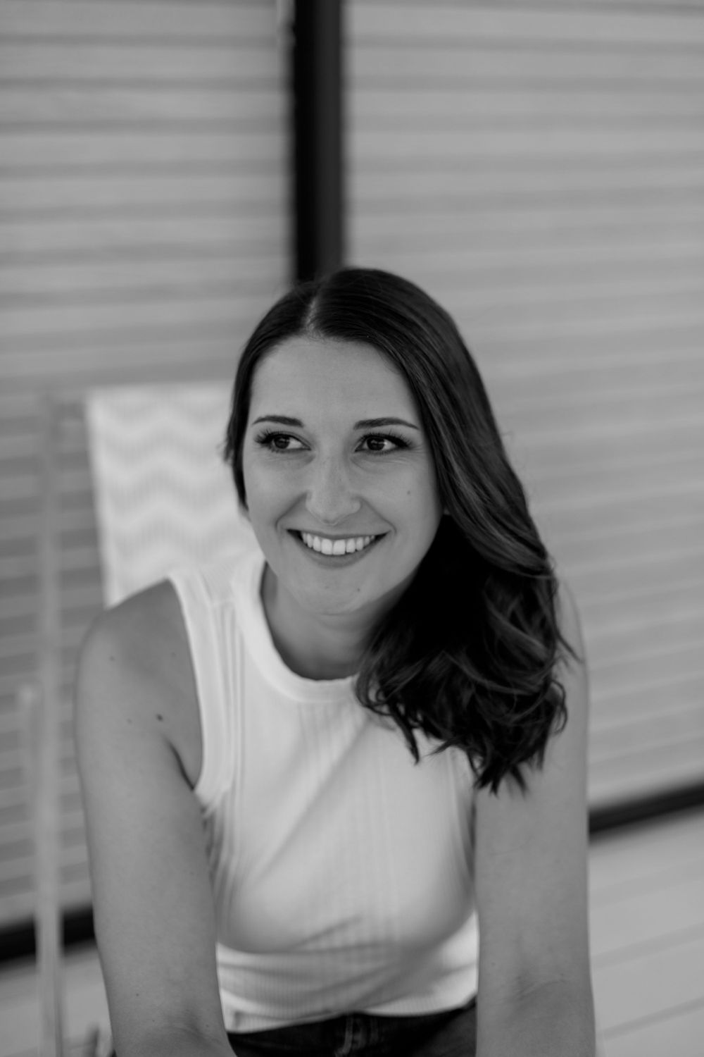 A black and white portrait of a smiling woman in a white sleeveless top with flowing dark hair.