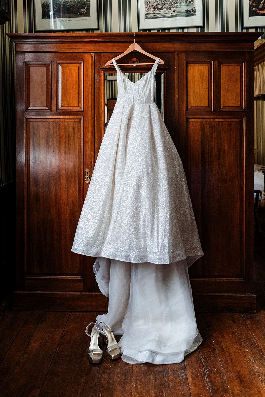 Elegant white wedding dress hanging on a wooden wardrobe with shoes beneath.