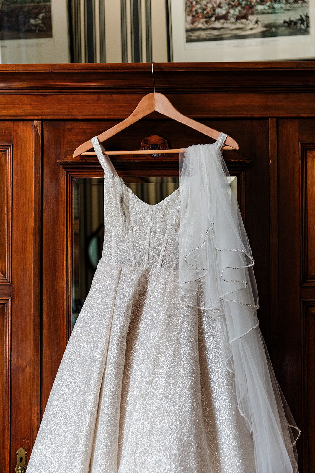Close-up of sparkly white wedding dress bodice and veil hanging on wooden hanger.