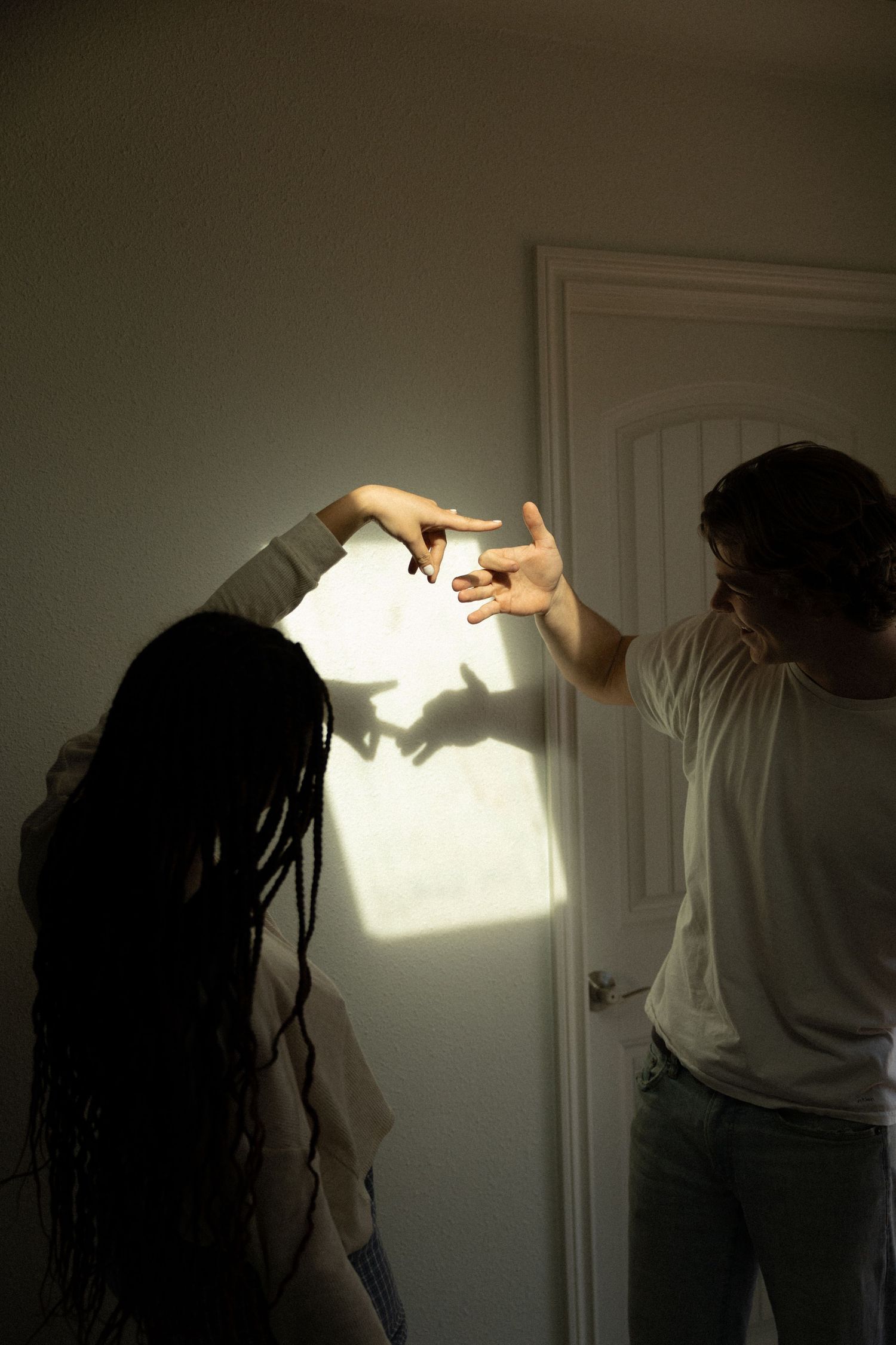 Two people create shadow puppets on a white wall using a bright light source.