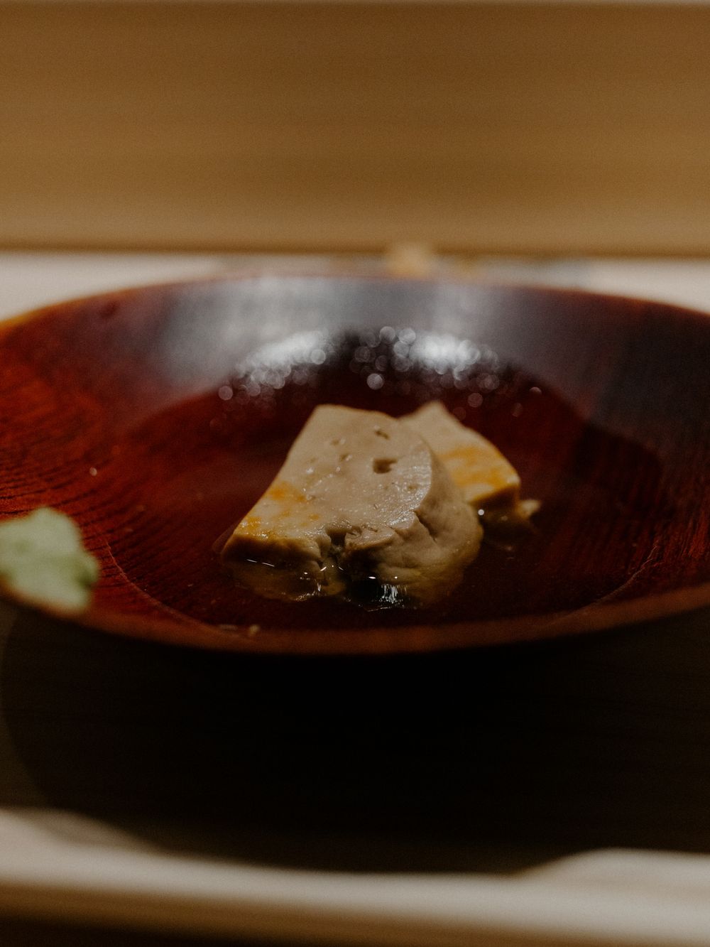 A delicate tofu dish served in a deep red lacquered bowl with minimal garnish.