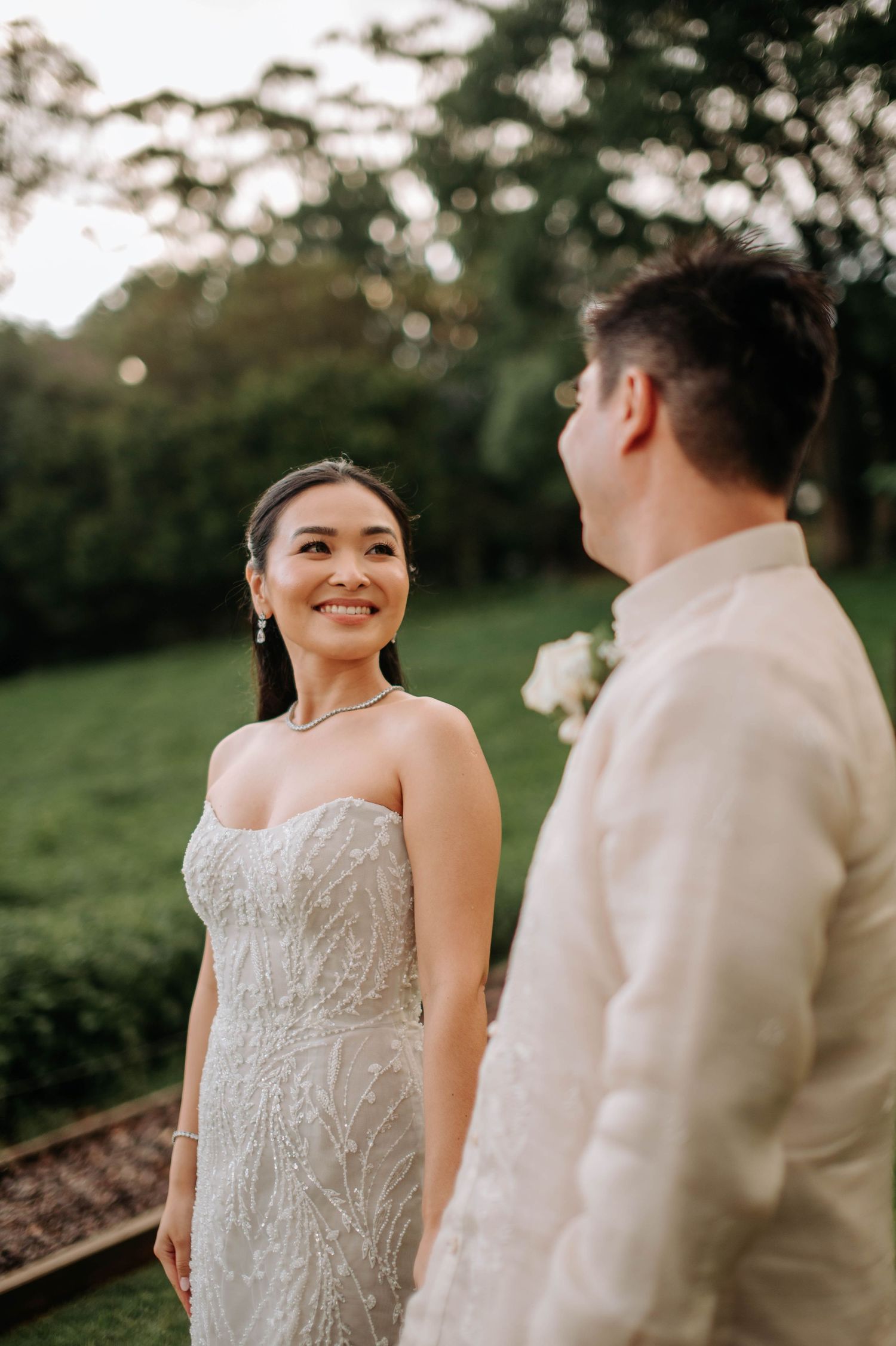 Couple in wedding attire sharing a romantic moment in a garden setting at sunset.