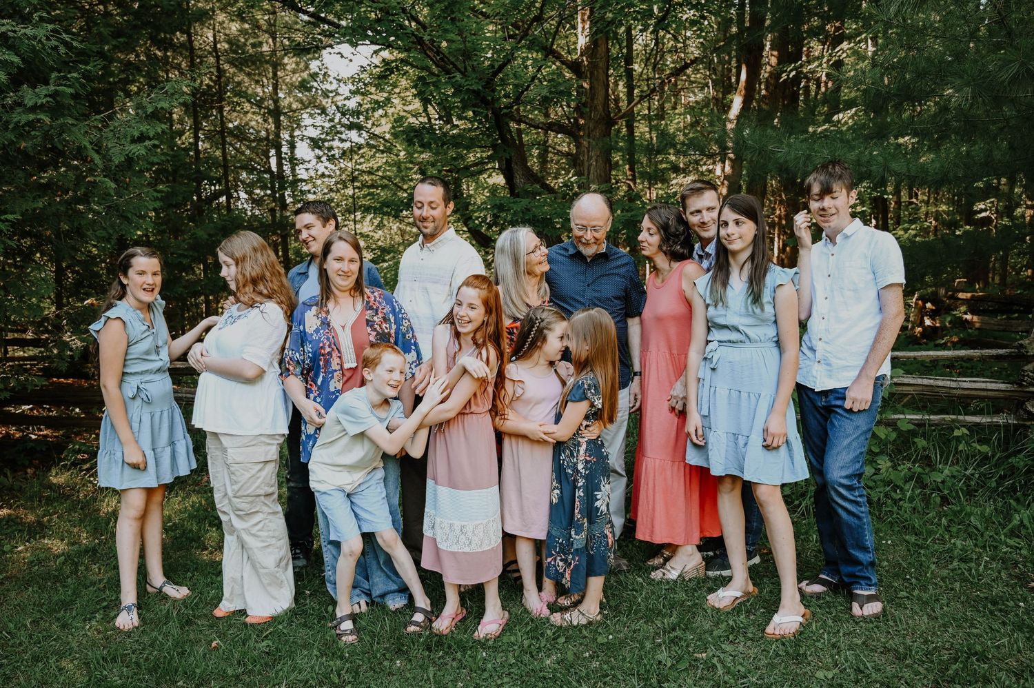A large family group poses together in a lush green outdoor setting wearing coordinated casual attire.