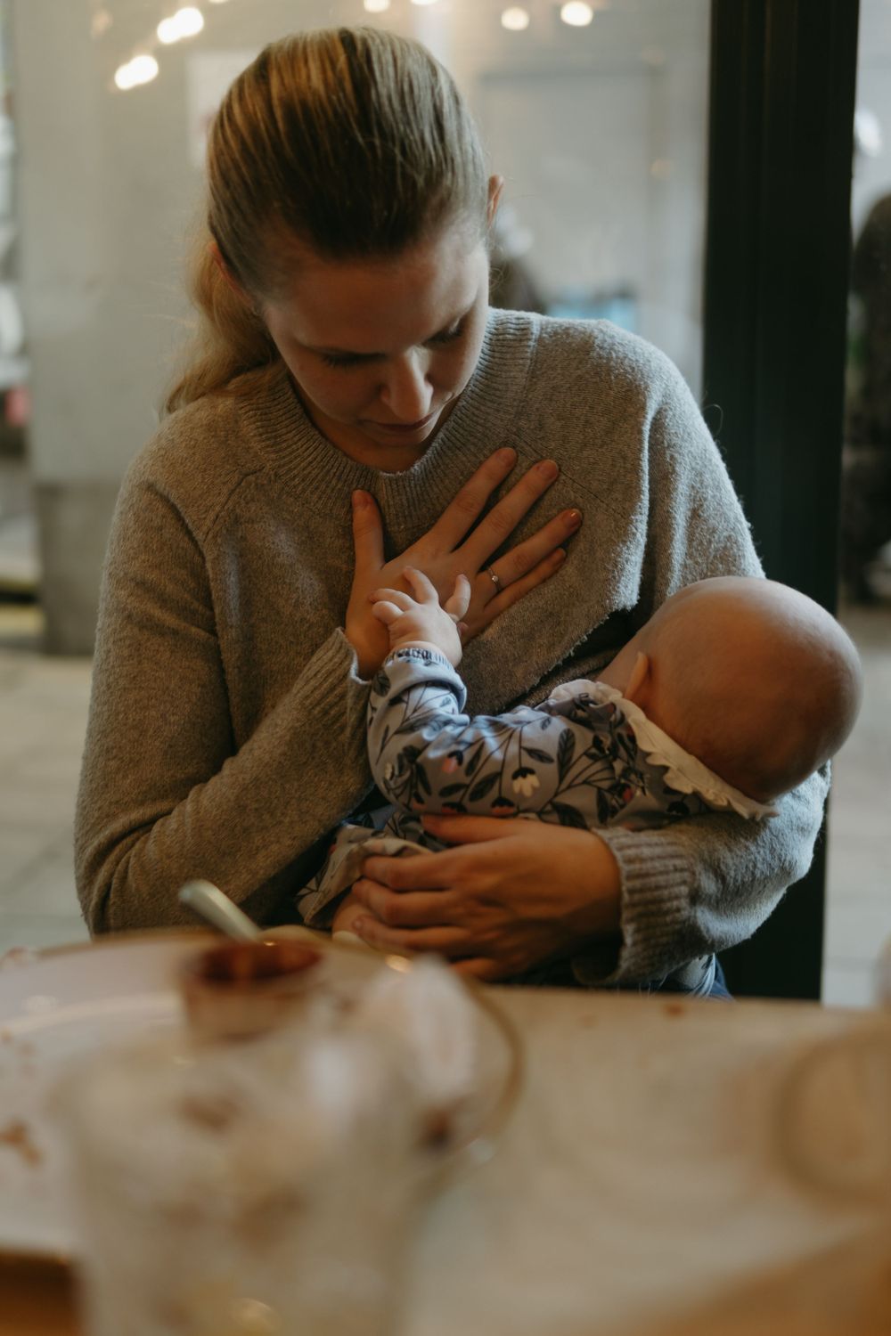 mother holding her baby with her hand placed on her heart being captured by lifestyle event photographer in Stockholm