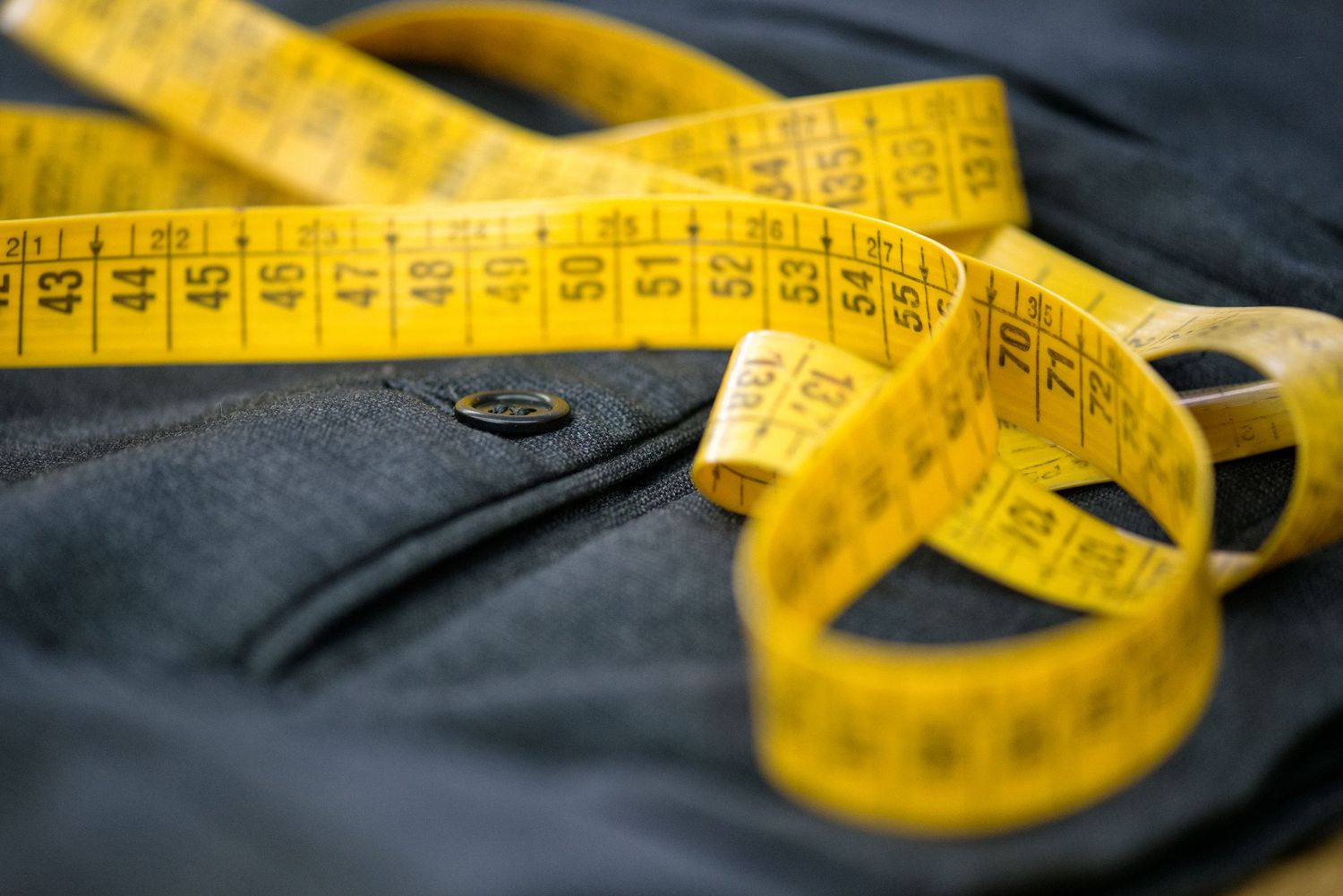 Yellow measuring tape laid across dark fabric showing measurement markings.
