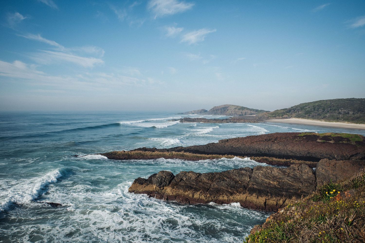 Dramatic coastal landscape with rocky cliffs and crashing waves against a blue sky along the Pacific coastline.