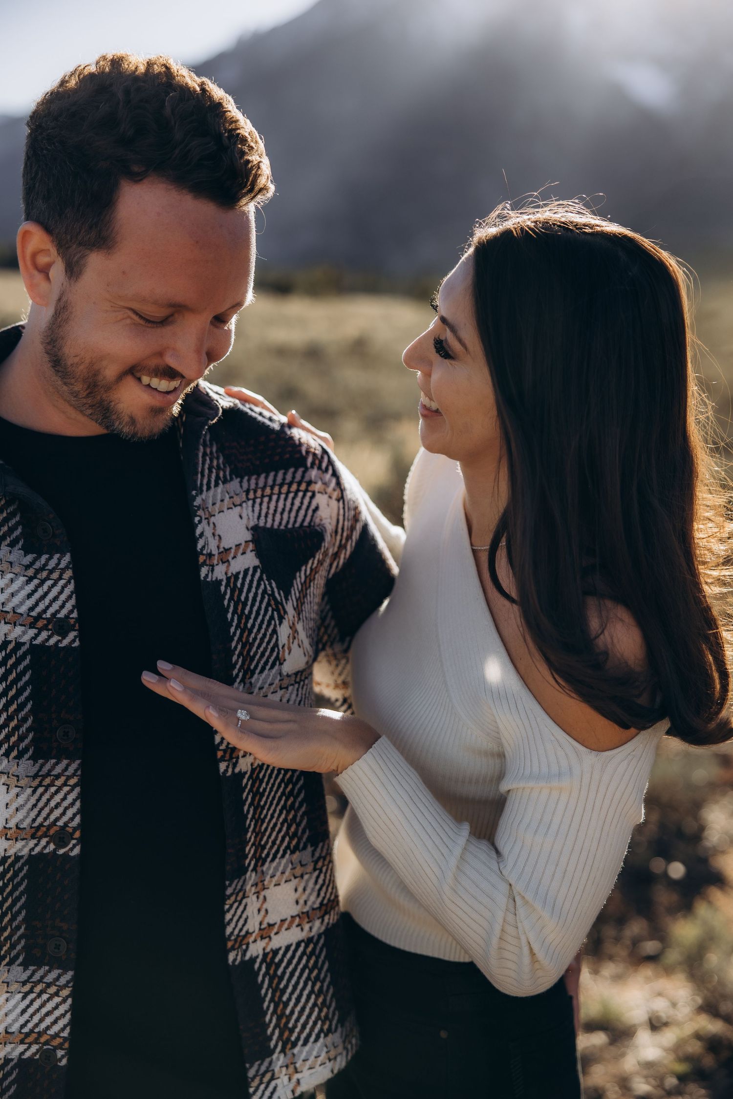 A couple shares a tender moment outdoors at sunset, with the person in a plaid shirt and another in white sweater.