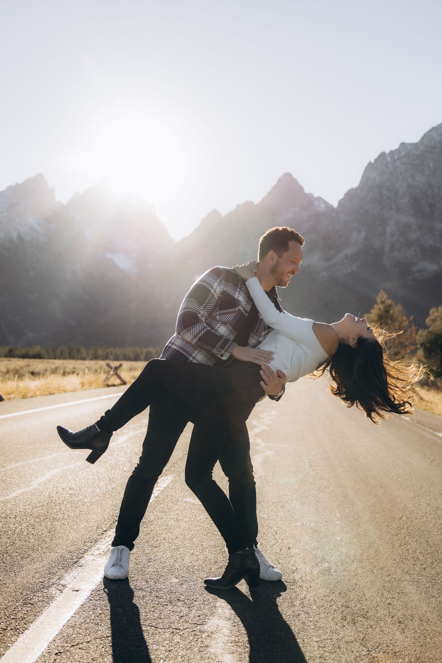 A couple dances and embraces on an empty mountain road during sunset with dramatic peaks in the background.