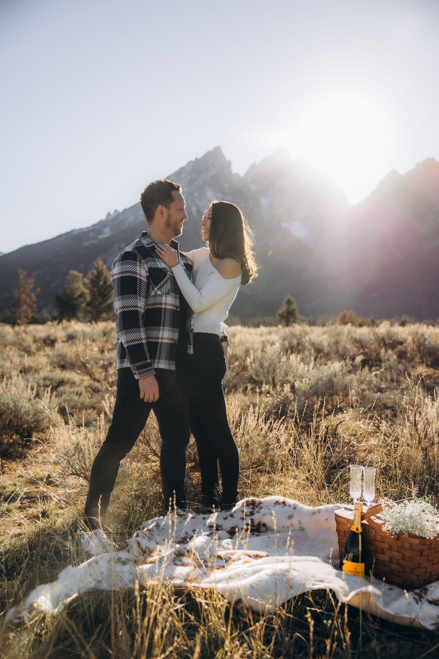 A romantic picnic setup with blanket and wine bottle in a mountain meadow at sunset with golden backlighting.