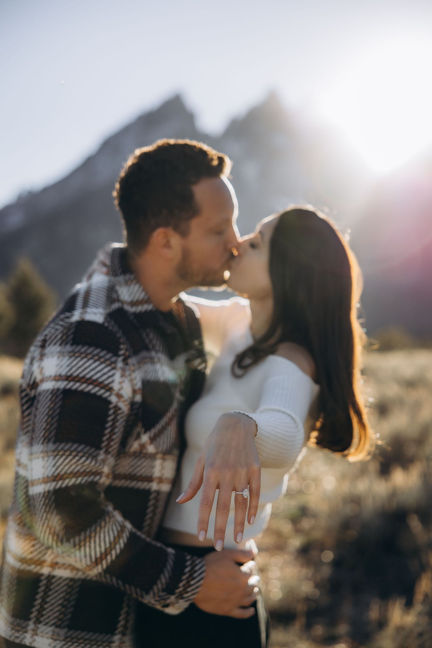 A couple shares a romantic moment in front of mountain scenery during golden hour sunset light.