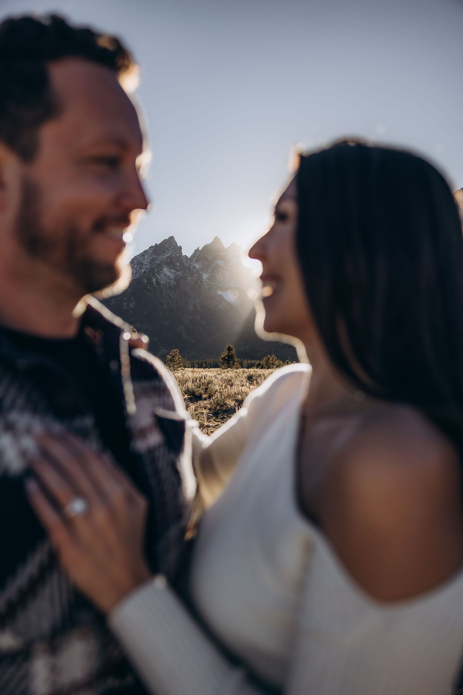 A romantic mountain engagement photo captured at sunset with the Grand Tetons silhouetted in the background.