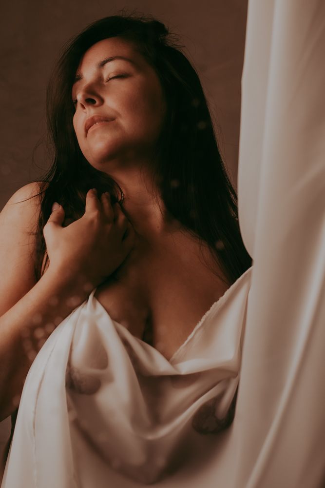 Sensuele boudoir foto van een vrouw met een witte doek voor haar lichaam gedrapeerd
