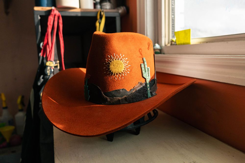 Orange cowboy hat with sun and cactus design sitting on windowsill.