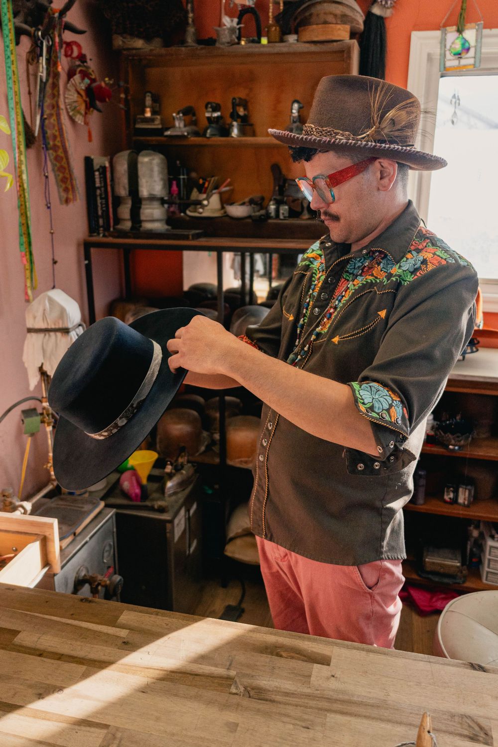 Craftsperson shaping a black cowboy hat in a workshop with orange walls.