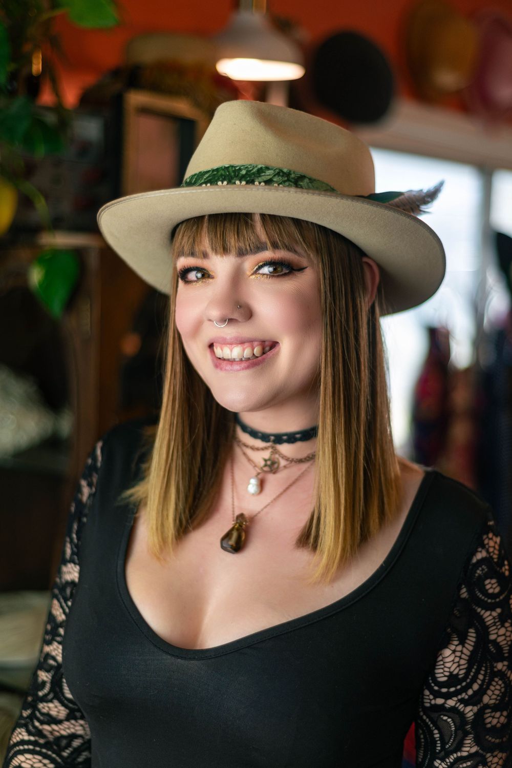 Portrait of person wearing cream fedora with feather detail and black lace top.
