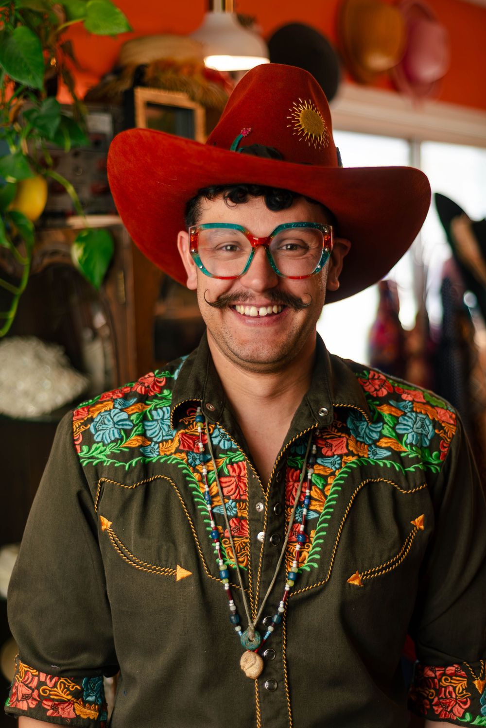 Person in vibrant embroidered western shirt and red cowboy hat smiling indoors.