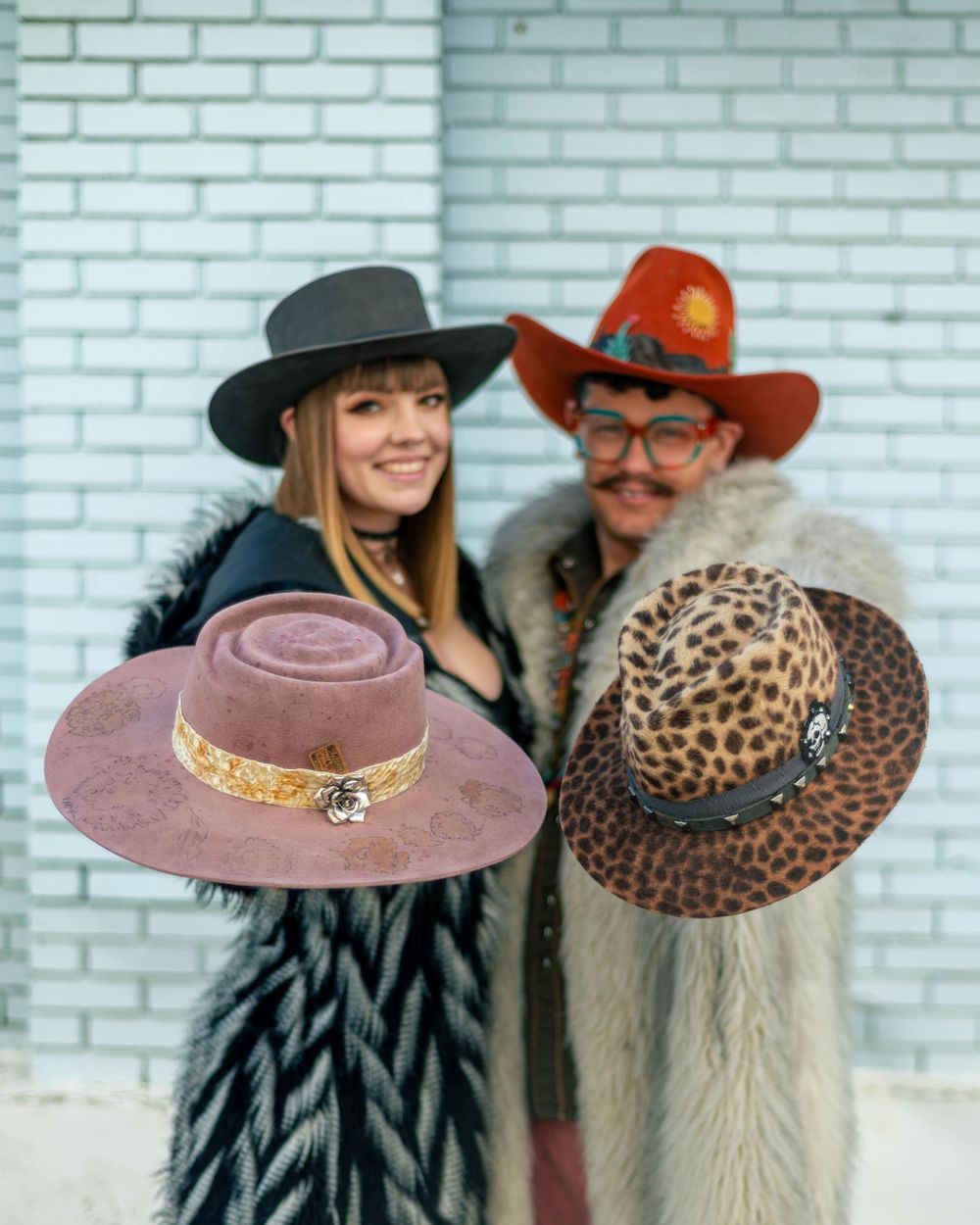 Western-styled portrait featuring colorful hats against white brick wall.