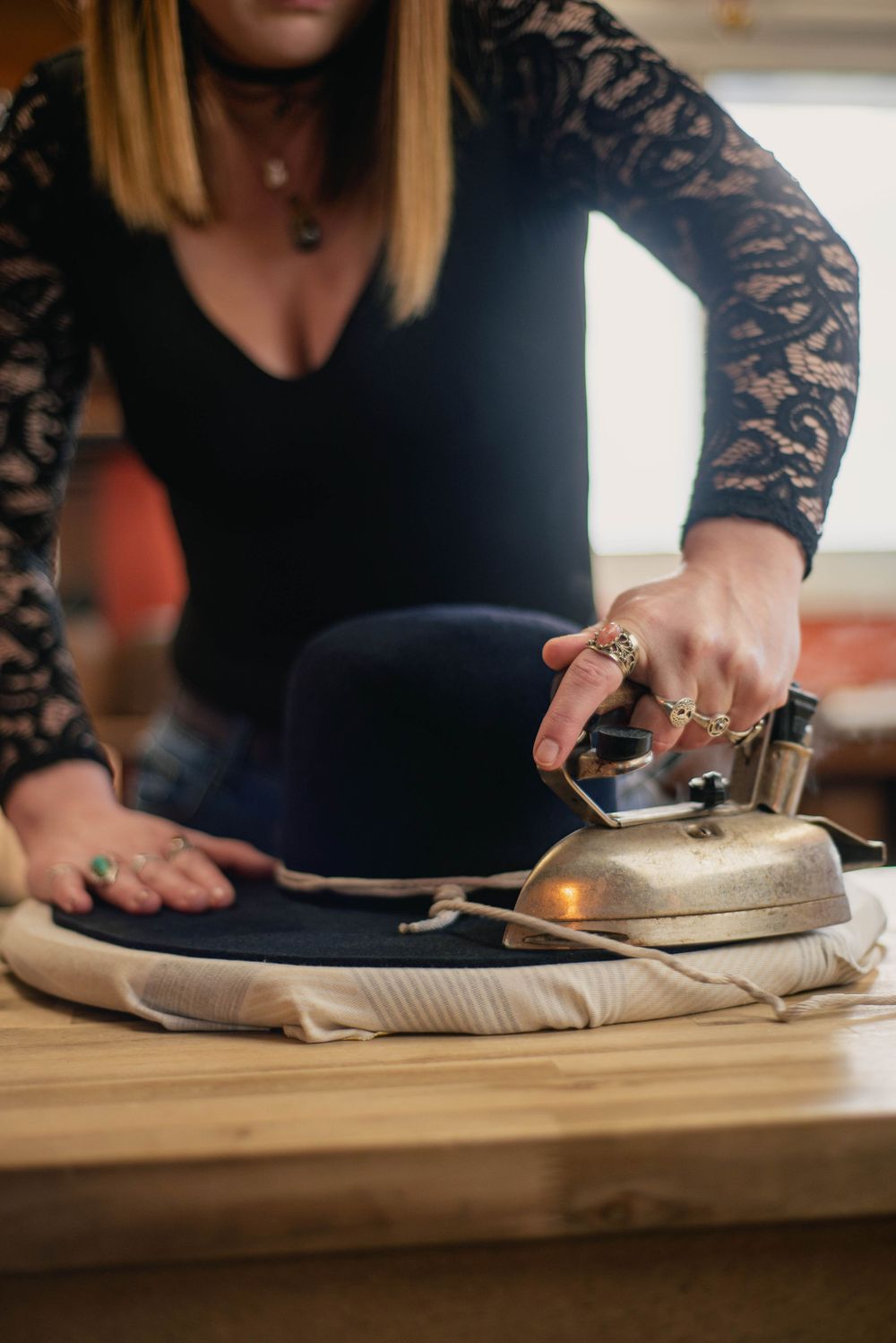 Close-up of hands steaming and shaping a navy blue hat on wooden table.