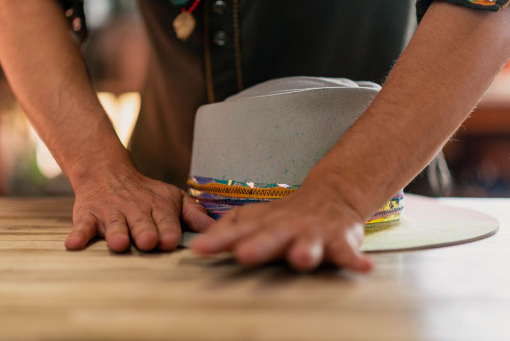 Close-up of hands working on a hat brim at a wooden workbench.