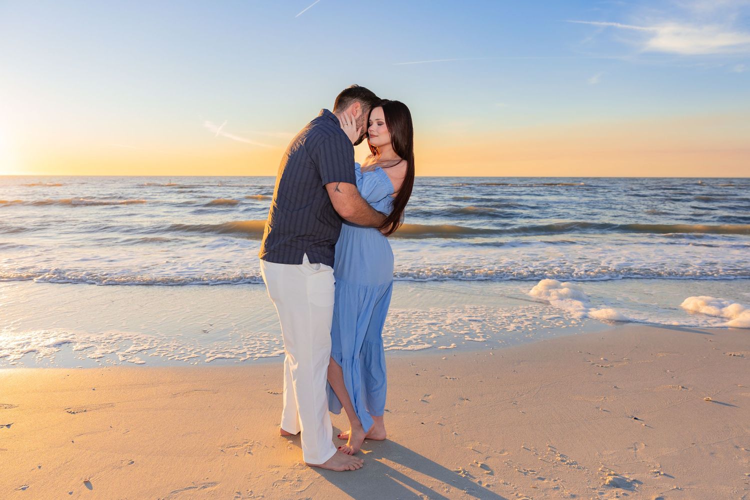 A couple shares a romantic moment on the beach at sunset as waves roll onto the sandy shore.