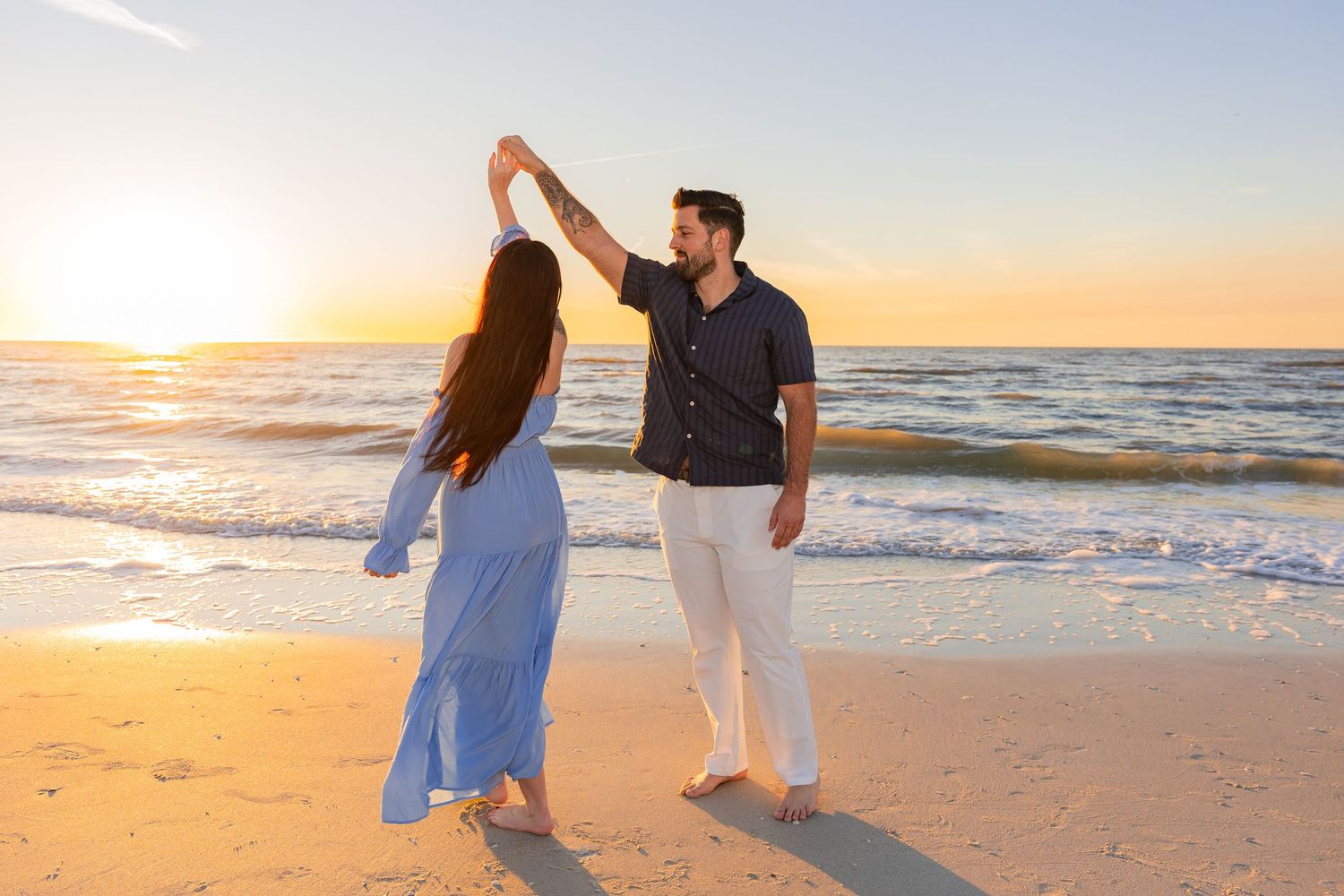 A couple walks hand in hand along a sandy beach at sunset with gentle waves rolling onto the shore.