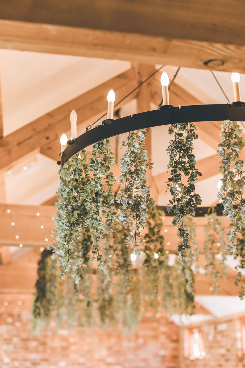 Elegant hanging greenery and fairy lights decorate rustic wooden wedding venue ceiling.