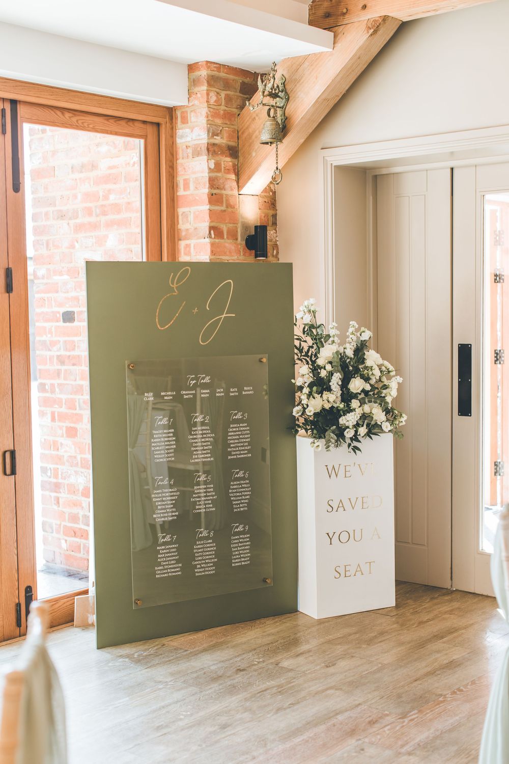 Olive green seating chart displays with floral accents in rustic venue.
