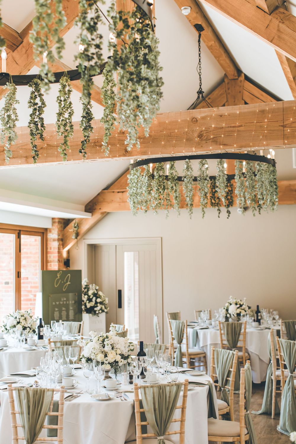 Rustic wedding reception venue with wooden beams and hanging greenery decorations.