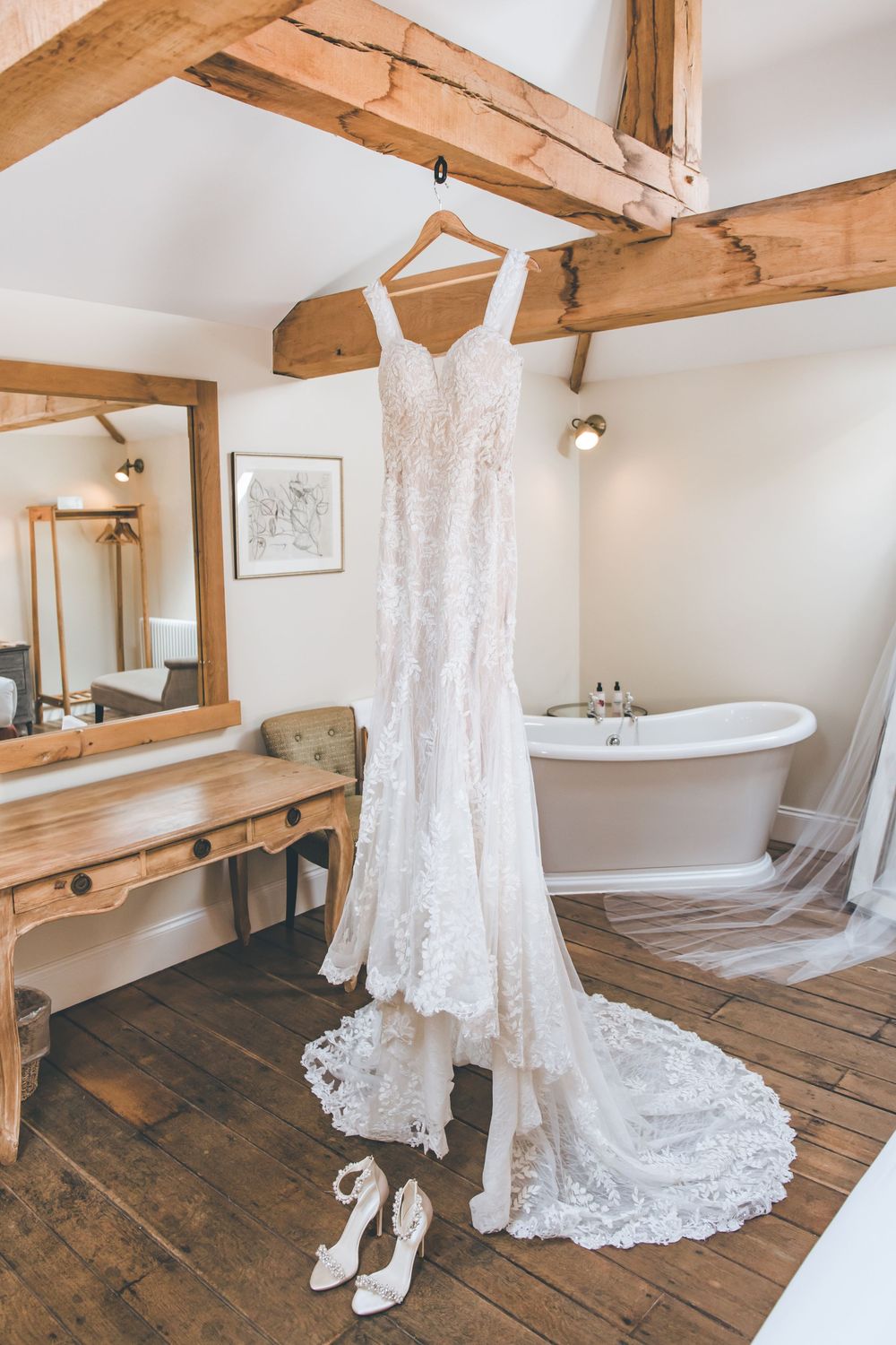 Wedding dress and accessories displayed in rustic room with wooden floors and freestanding bathtub.