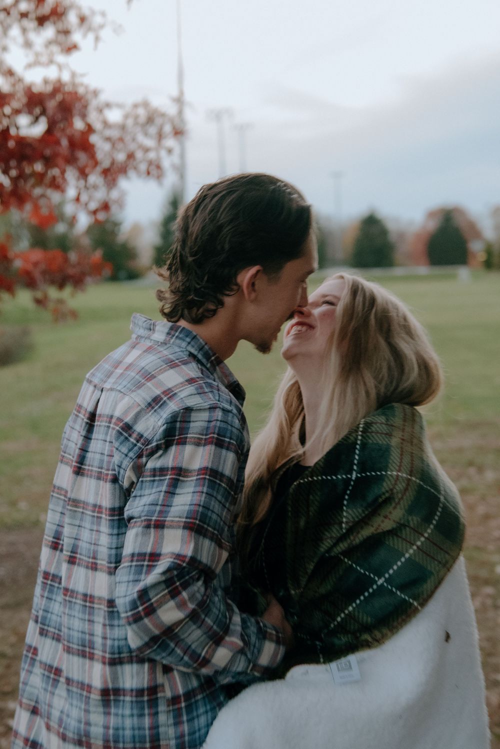 A romantic autumn moment between a couple wrapped in a blanket outdoors.