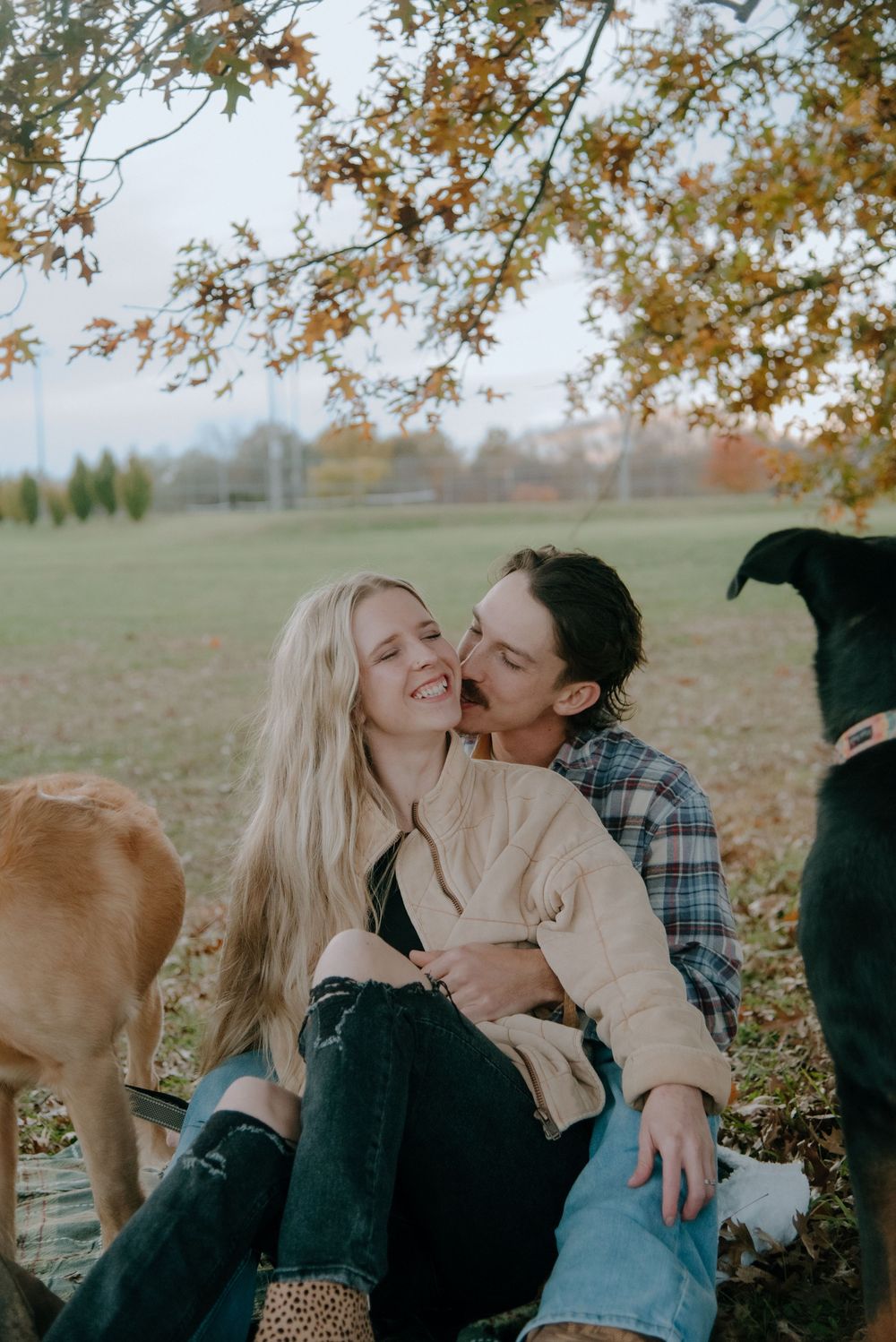 A couple laughing together outdoors with their dogs during autumn.